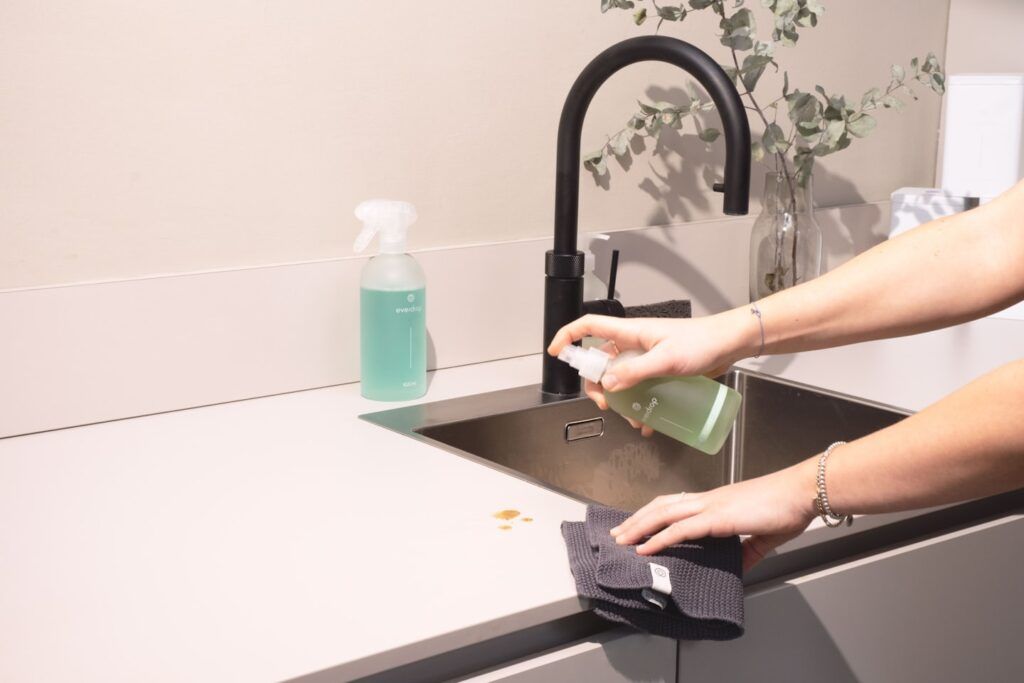 Une mainqui pulvérise du produit sur un plan de travail avec une éponge dans l'autre main
